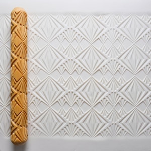 May include: A wooden rolling pin with a carved geometric pattern. The pattern is a repeating diamond shape with a fan-like design inside each diamond.
