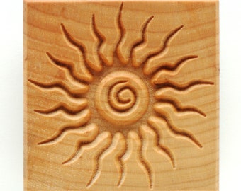 May include: A wooden sun-shaped stamp with a carved spiral design in the center. The stamp is made of light wood and has a natural finish.