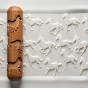 May include: A wooden rolling pin with a carved design of running horses. The rolling pin is approximately 15 cm long and 5 cm in diameter. The design is repeated on the rolling pin, with each horse facing the same direction.