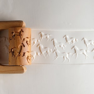 Könnte beinhalten: Ein Nudelholz aus Holz mit einem geschnitzten Muster von rennenden Pferden. Das Nudelholz wird verwendet, um geprägte Muster in Teig zu erstellen.
