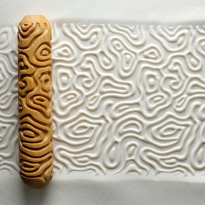 May include: A wooden rolling pin with a carved pattern of swirling lines. The rolling pin is used to create a textured design on clay or dough.