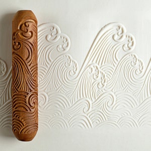 May include: A wooden rolling pin with a carved design of waves. The rolling pin is brown and has a natural wood finish. The design is intricate and detailed, and the waves are flowing and dynamic.