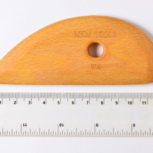 May include: A wooden sculpting tool with a rounded, curved shape. The tool is approximately 8 inches long and has a hole in the center. The tool is labeled "MXM TOOLS" and "W4".