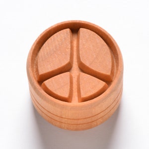May include: A wooden peace sign carved into a round wooden block. The block has a natural wood finish.