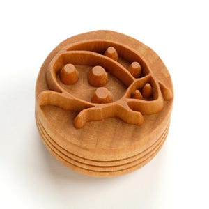 Könnte beinhalten: Ein runder Holzstempel mit einem geschnitzten Marienkäfer-Design. Der Stempel ist hellbraun und weist ein detailliertes Relief des Insekts auf, einschließlich seiner Punkte und Körperform. Der Stempel besteht aus geschichtetem Holz und eignet sich für Bastelarbeiten.