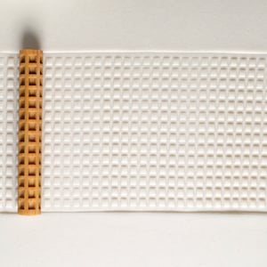 May include: A brown rolling pin with a waffle-like texture sits on a white surface with a raised grid pattern.