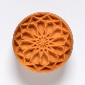 May include: A round, brown, decorative mold with a geometric pattern. The mold has a raised, intricate design that resembles a flower.