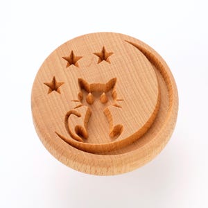Peut inclure: Tampon rond en bois clair avec un motif sculpté d'un chat assis sur un croissant de lune et trois étoiles. L'objet est probablement utilisé pour l'artisanat ou la pâtisserie. Le diamètre est d'environ 7,6 cm.