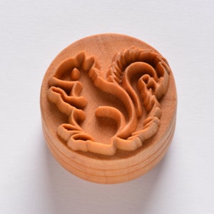 May include: A wooden stamp with a detailed carving of a squirrel. The stamp is round and has a light brown color.
