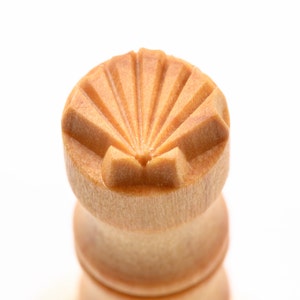 Op de afbeelding: Een close-up van een houten schaakstuk met een gesneden schelpontwerp op de bovenkant. Het stuk is lichtbruin van kleur en heeft een gladde, gepolijste afwerking.