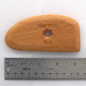 May include: A wooden sculpting tool with a rounded shape and a hole in the centre. The tool is labelled "MKM TOOLS" and "W10".