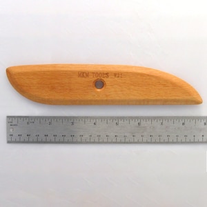 May include: A wooden sculpting tool with a rounded edge and a hole in the center. The tool is labeled "MKM TOOLS W21".