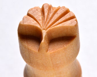 May include: A wooden stamp with a carved design of a stylized leaf. The stamp is light brown and has a rounded top.
