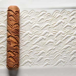 May include: A wooden rolling pin with a carved design of waves. The rolling pin is used to create decorative patterns in clay or fondant.
