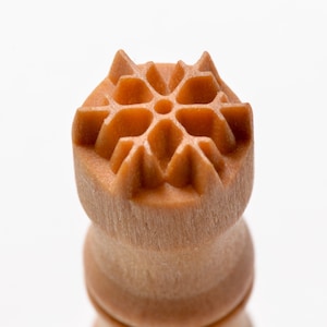 May include: A wooden stamp with a detailed snowflake design. The stamp is brown and has a rounded top.