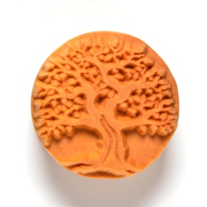 May include: A round, orange-brown rubber stamp with a raised design of a tree with branches and leaves.