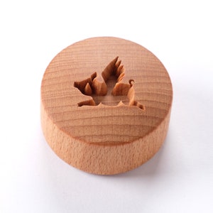 May include: A round wooden stamp with a carved design of a bird in flight. The stamp is made of light brown wood and has a smooth surface.