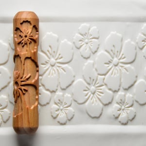 May include: A wooden rolling pin with a floral design. The rolling pin is made of natural wood and has a smooth, polished finish. The floral design is carved into the rolling pin and features delicate flowers and leaves.