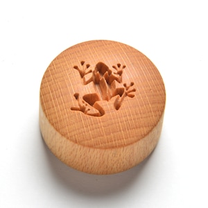 May include: A round wooden button with a carved frog design.