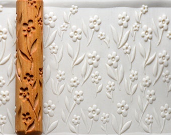 May include: A wooden rolling pin with a floral design. The rolling pin is used to create decorative patterns in clay or dough.