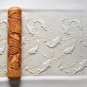 May include: A wooden rolling pin with a carved design of fish and waves. The rolling pin is brown and has a natural wood finish. The design is intricate and detailed.