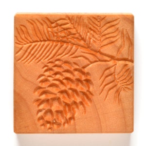 Puede incluir: Una talla de madera de una piña y una rama. La talla es de color marrón claro y tiene un diseño detallado.