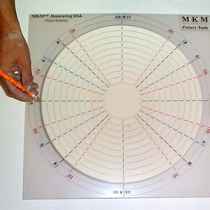 May include: A white circular decorating disk with concentric circles and radial lines in red, blue, and green. The disk is labeled "MKM™ Decorating Disk (Patent Pending!)" and "MKM Pottery Tools".