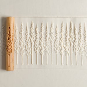 May include: A wooden rolling pin with a carved design of a forest of pine trees. The rolling pin is used to create an embossed pattern on dough or fondant.