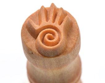 May include: A wooden stamp with a hand and spiral design. The stamp is made of light brown wood and has a smooth surface.