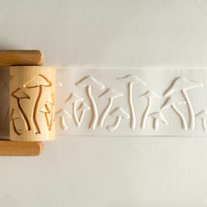 May include: A wooden rolling pin with a carved mushroom design. The rolling pin is used to create an embossed pattern on clay or dough.