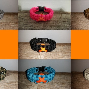 May include: Assortment of paracord bracelets with an orange ribbon charm. The bracelets are in various colors, including gray, pink, black, teal, and beige.