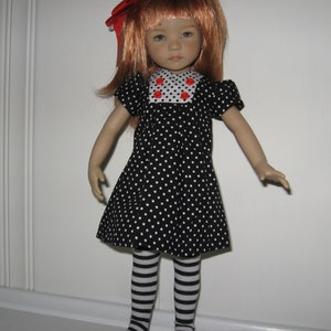 May include: A doll with red hair and a red bow. The doll wears a black dress with white polka dots, a white collar with red polka dots, and black and white striped stockings. The doll's arms are outstretched.