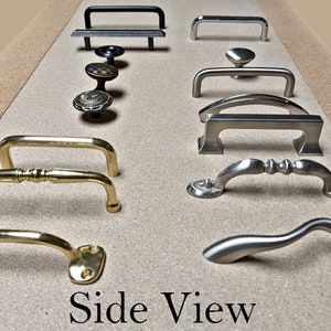 May include: A collection of cabinet hardware, including handles and knobs, in various styles and finishes. The hardware includes black, silver, and gold tones. The image is labeled "Side View".