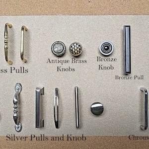 May include: A collection of cabinet hardware, including brass pulls, antique brass knobs, a bronze knob and pull, a black pull, silver pulls and a knob, and a chrome pull. The hardware is displayed on a neutral background.