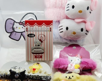 May include: A collection of Hello Kitty themed accessories, including plush toys, hair ties, and a box set. The plush toys feature Hello Kitty with pink bows. The hair ties have various character designs. The box set has the text "HELLO KITTY" and Japanese text.
