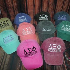 Puede incluir: Nueve gorras de b&eacute;isbol de diferentes colores con varias letras griegas y nombres bordados en ellas. Las gorras est&aacute;n hechas de un material suave y c&oacute;modo y son perfectas para mostrar el esp&iacute;ritu de tu escuela.