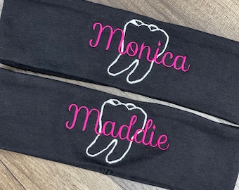 May include: Two black headbands with white tooth designs and pink embroidered names. The top headband says "Monica" and the bottom headband says "Maddie".