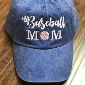 May include: A blue baseball cap with white embroidery that reads "Baseball MOM" with a white baseball with red stitching in the center.