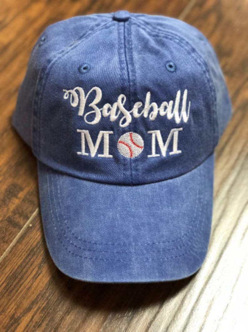 May include: A blue baseball cap with white embroidery that reads "Baseball MOM" with a white baseball with red stitching in the center.