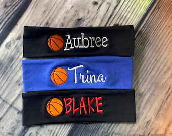 May include: Three fabric headbands featuring embroidered basketball icons and personalised names. The top headband is black with white text reading Aubree, the middle is blue with white text reading Trina, and the bottom is black with red text reading BLAKE.