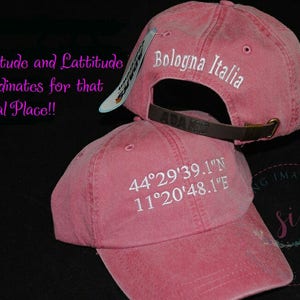 May include: Two pink baseball caps with white embroidery. The top cap says "Bologna Italia". The bottom cap says "44&deg;29'39.1"N 11&deg;20'48.1"E".