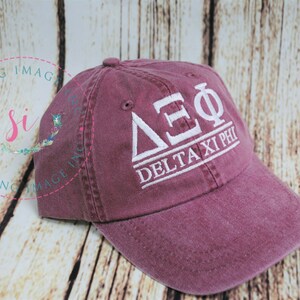 Puede incluir: Una gorra de b&eacute;isbol de color granate con bordado blanco que dice "&Delta;&Sigma;&Phi; Delta Xi Phi".