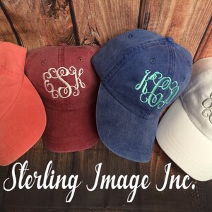 May include: Four different colored baseball caps with embroidered monograms. The caps are in shades of red, blue, white, and coral. The monograms are in white, silver, and teal.