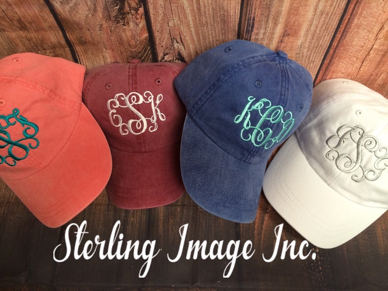 May include: Four different colored baseball caps with embroidered monograms. The caps are in shades of red, blue, white, and coral. The monograms are in white, silver, and teal.