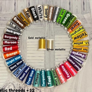 May include: A variety of embroidery floss spools arranged in a circle, with colors including black, white, ivory, rainbow, cotton candy, lime green, green, kiwi green, coral, highlighter yellow, light yellow, sun yellow, purple, lavender, royal purple, neon pink, fuchsia, light pink, mint green, teal, turquoise, tiffany, true blue, royal blue, light blue, navy blue, bright blue, orange, red, maroon, burgundy, dark grey, light grey, brown, tan, vegas gold, gold metallic, and silver metallic. The text "Metallic threads + $2" is at the bottom of the image.