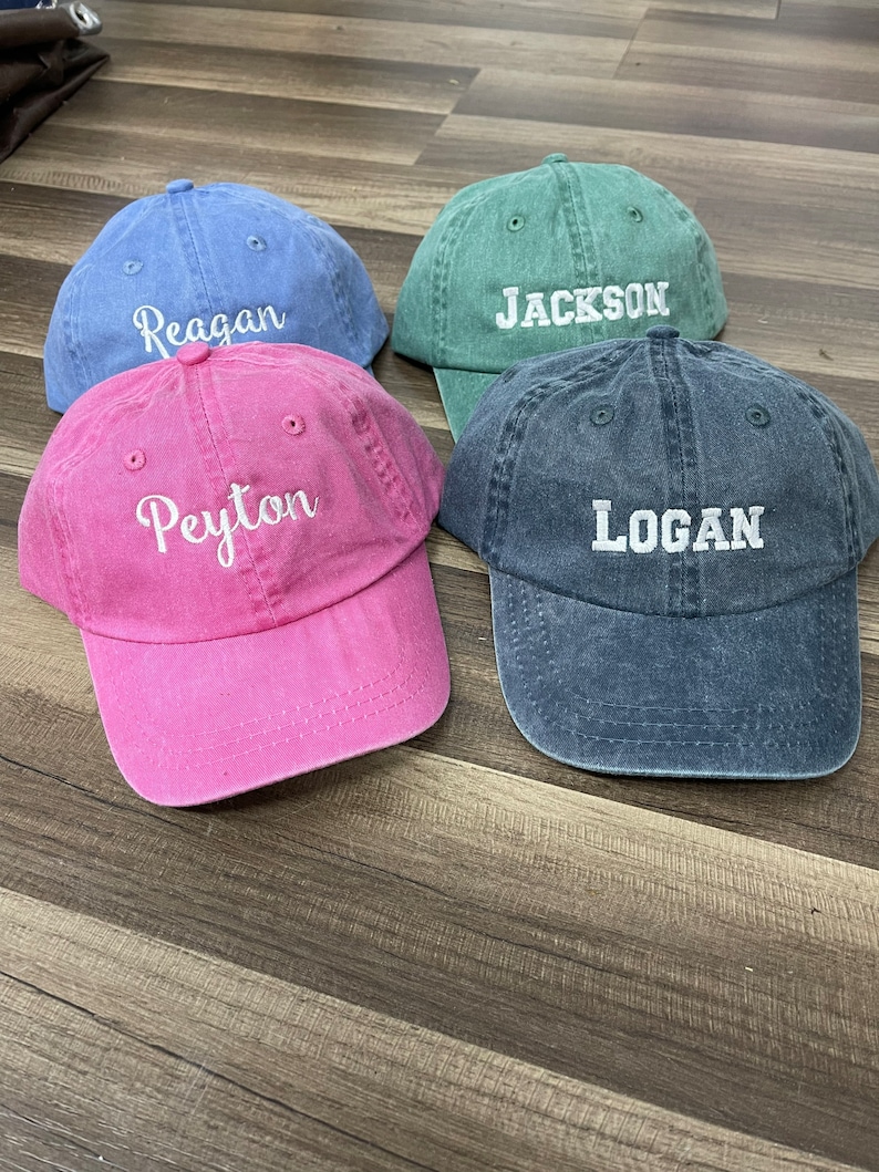 May include: Four denim baseball caps in different colors with embroidered names: Reagan, Peyton, Jackson, and Logan.