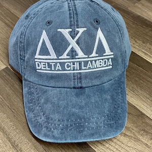 May include: A blue denim baseball cap with white embroidered lettering that reads "ΔΧΛ DELTA CHI LAMBDA".