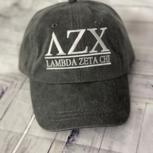 May include: A dark gray baseball cap with white embroidered lettering that reads "ΛZX Lambda Zeta Chi".