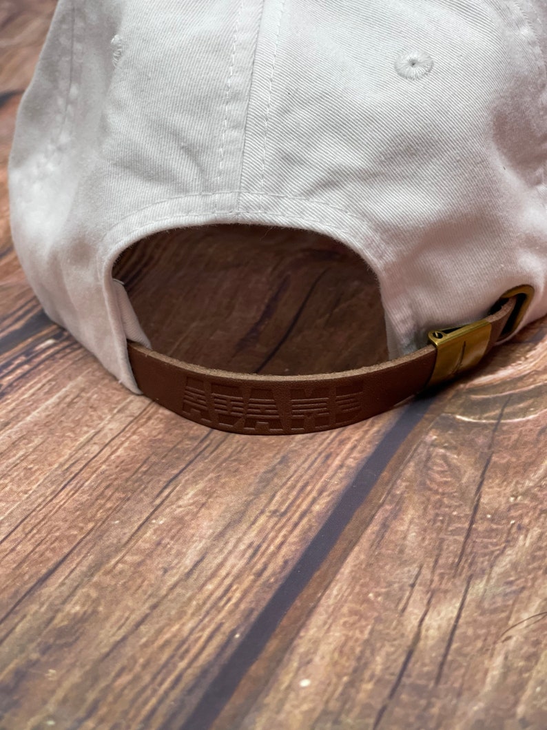 May include: White baseball cap with a brown leather strap that says "PALM" in raised lettering.