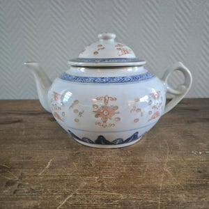 May include: A white porcelain teapot with a blue and gold floral design. The teapot has a lid and a handle.